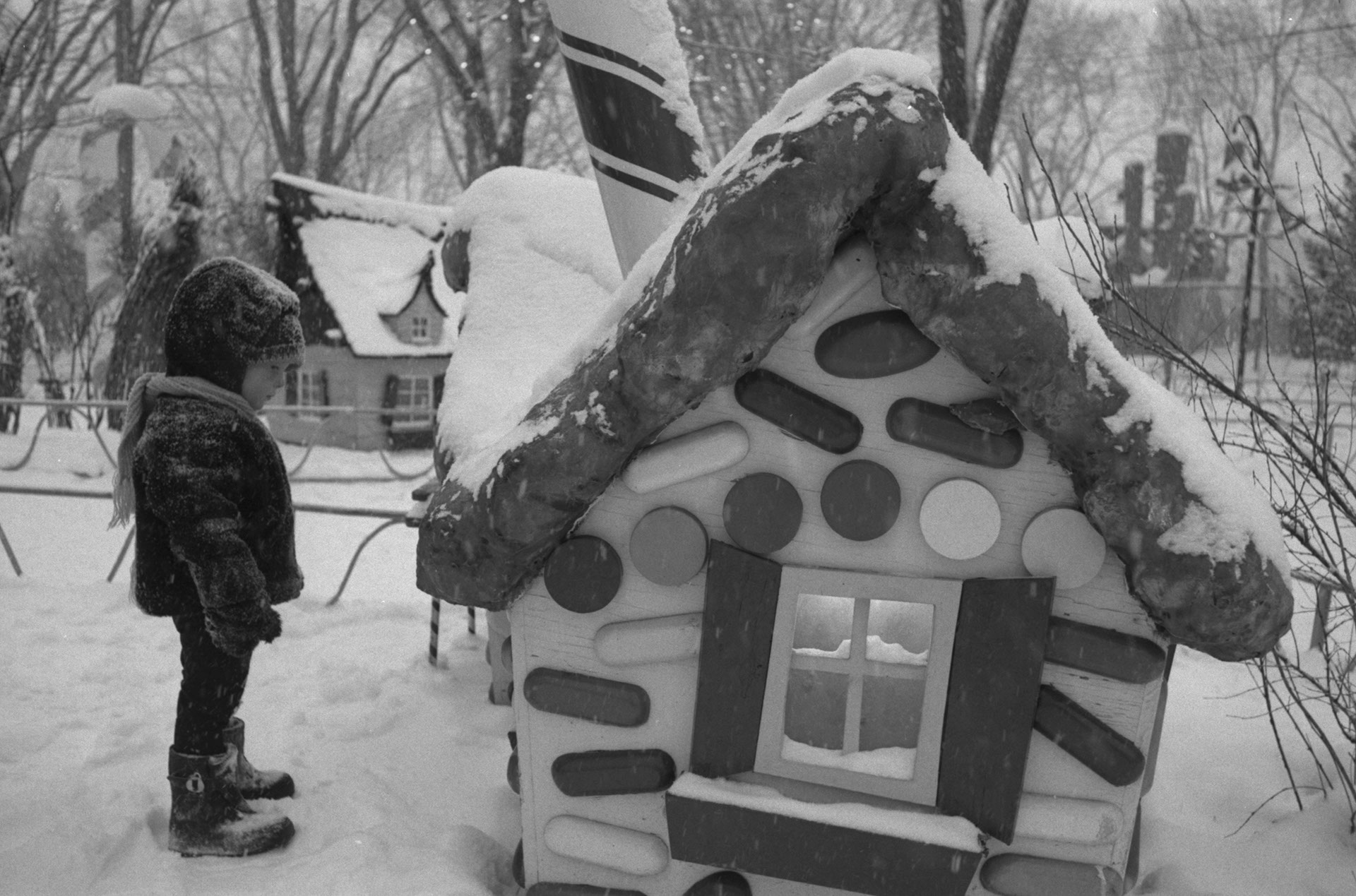 Small child in winter clothing looking at a candy-cane cottage