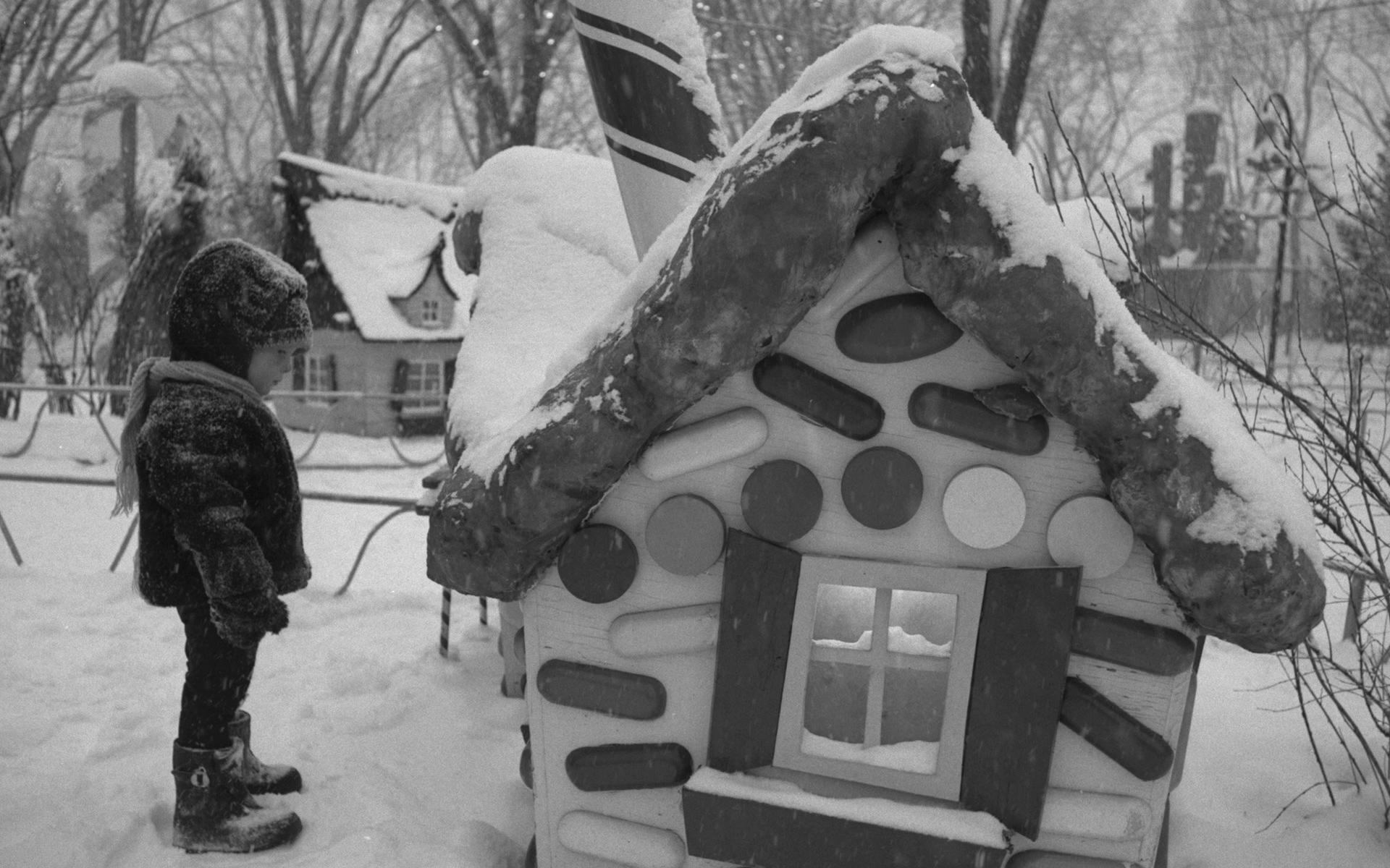 Small child in winter clothing looking at a candy-cane cottage